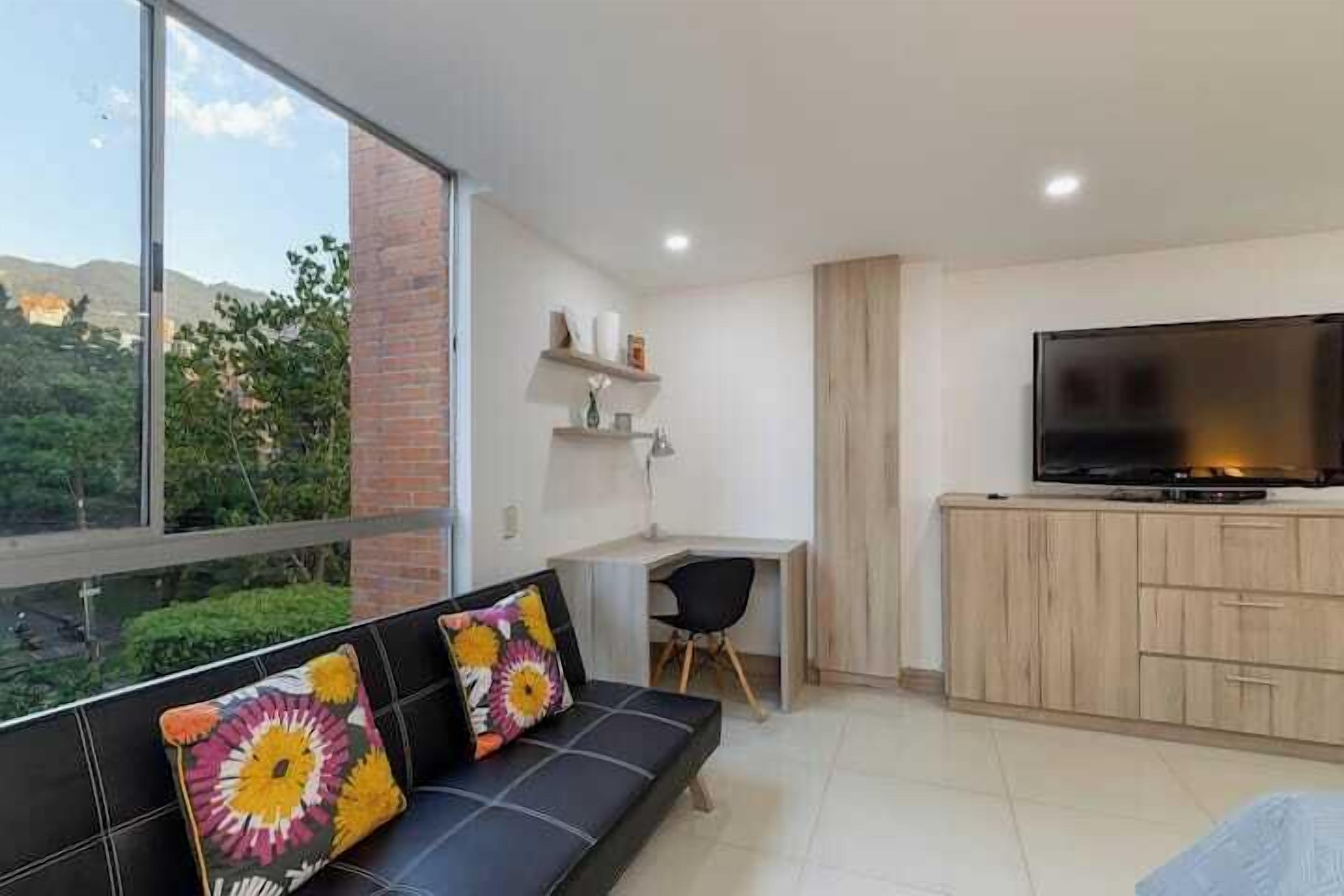 Uma sala de estar moderna com sofá, televisão, escrivaninha e vista para o verde.
