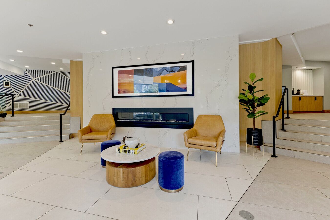 Un hall d’entrée moderne avec une cheminée, deux fauteuils, une table basse et un grand tableau abstrait.