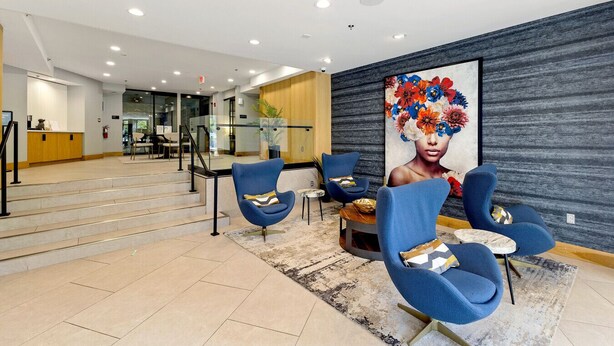 Un vestíbulo moderno con una escalera, sillones azules, una gran obra de arte floral y un mostrador de recepción.