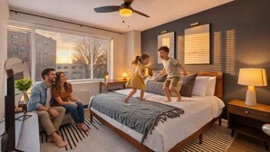Un dormitorio moderno con una cama grande, un ventilador de techo, una mesita de noche con lámpara y una ventana con persianas.