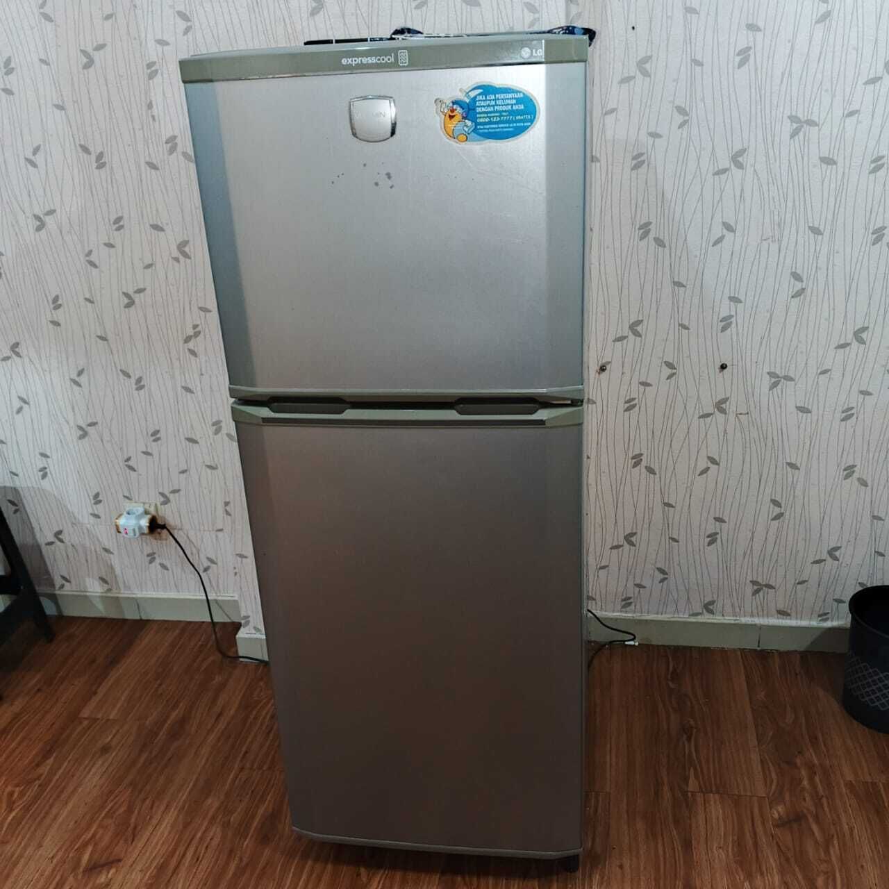 A refrigerator with a sticker and a power cord plugged into a wall socket.