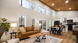 A spacious living area with a brown sofa, a coffee table, and a dining table with chairs. There is a kitchen area with white cabinets and a microwave. - Private | Hot Tub | Stargazing | Mountain View (Stanton)
