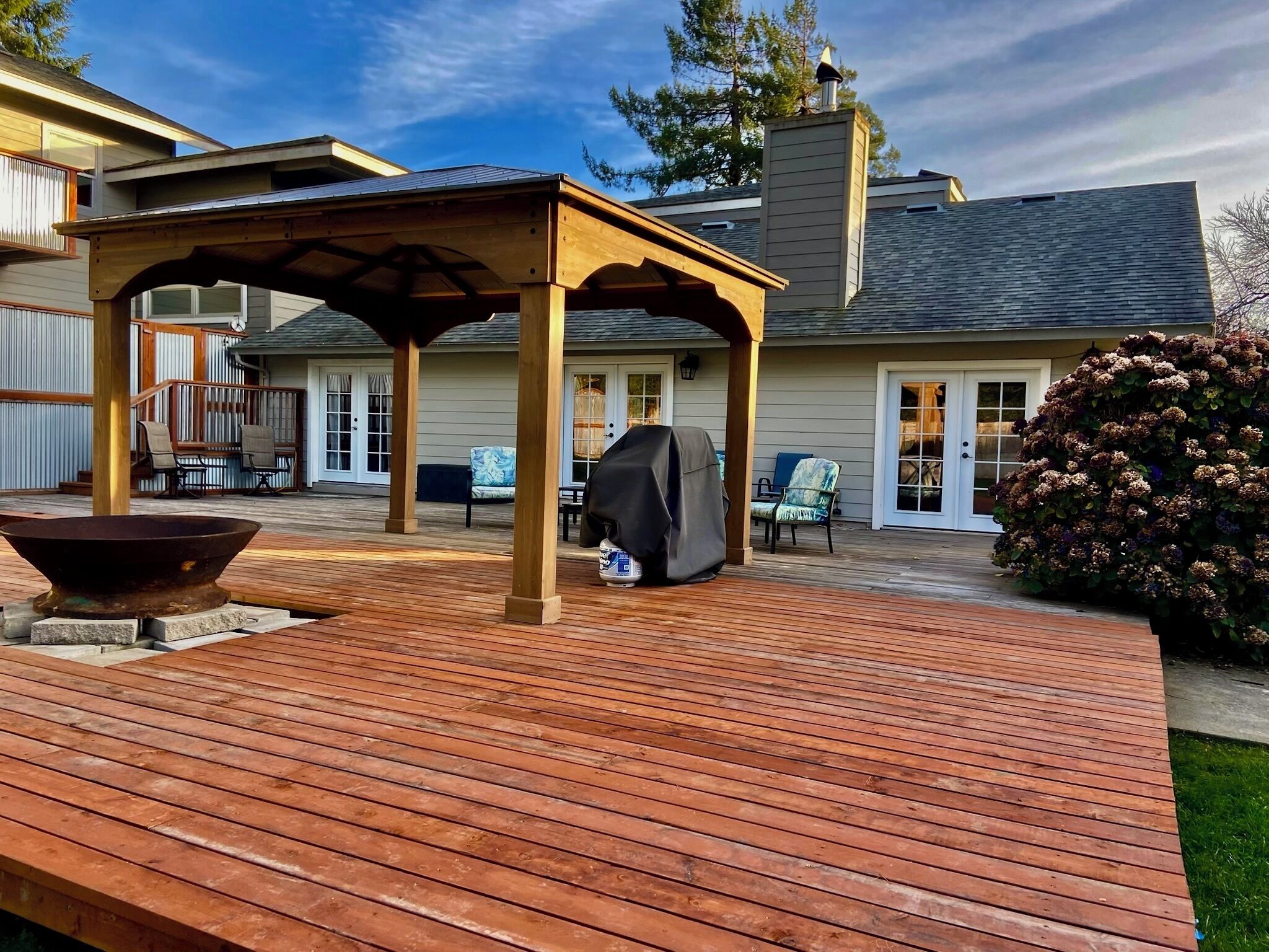A wooden deck with a pergola, outdoor seating, and a barbecue grill.