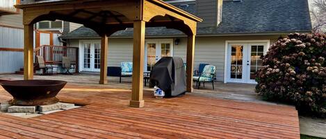 A wooden deck with a pergola, outdoor seating, and a barbecue grill.