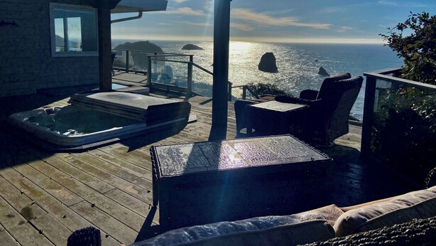 Een houten terras met een jacuzzi, tuinmeubilair en uitzicht op de oceaan.