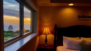 A hotel room with a bed, a nightstand with a lamp, a window with a view of the sea, and a wall sign. - Trinidad Coastal Retreat – Open Living, Panoramic Ocean Views & Stylish Comfort (Trinidad)