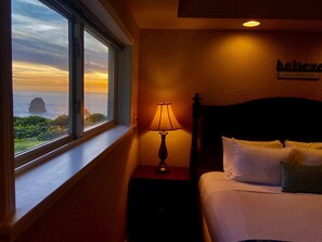 Quarto de hotel com cama, mesa de cabeceira com abajur, janela com vista para o mar e um letreiro na parede.