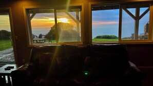A room with a view of the sunset over the ocean, a wooden deck outside, and a leather sofa inside. - Trinidad Coastal Retreat – Open Living, Panoramic Ocean Views & Stylish Comfort (Trinidad)