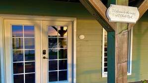 A wooden door with a glass panel, a sign reading "Welcome to the suites at Whale Rock," and a small plant in a pot. - Ocean-view studio near redwoods and beaches—your basecamp for Trinidad adventure. (Trinidad)