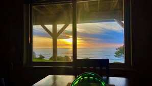 A room with a view of the sunset over the ocean, a wooden table, and a green object on the table. - Ocean-view studio near redwoods and beaches—your basecamp for Trinidad adventure. (Trinidad)