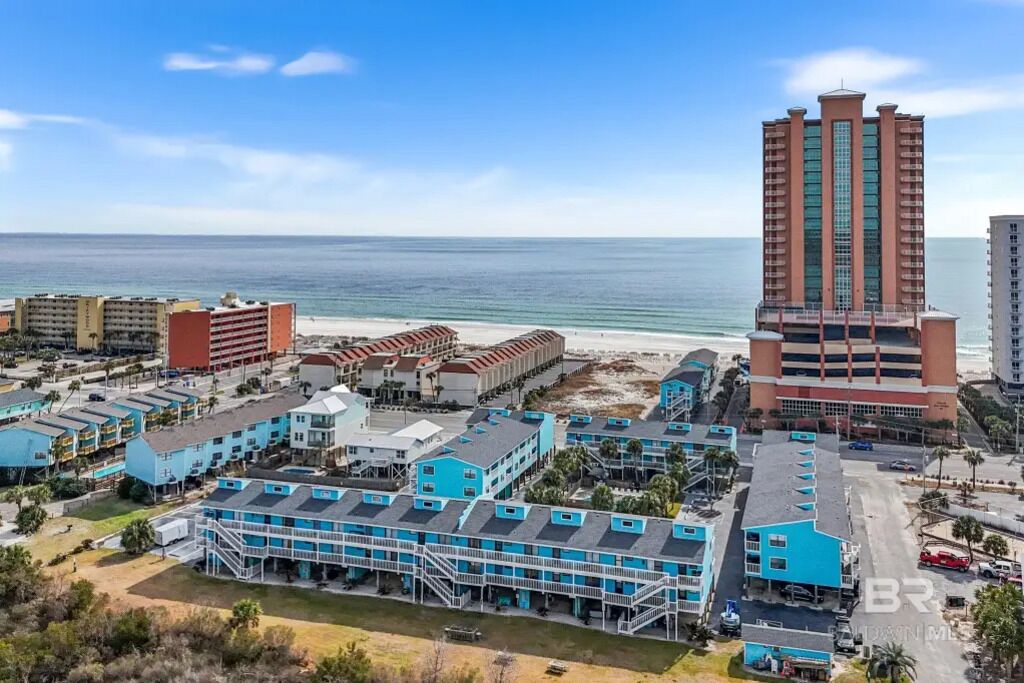 Ein Küstenhotelkomplex mit mehreren Gebäuden, darunter ein hohes Hotel mit roter und beiger Fassade sowie einige kleinere Bauten mit blauen Dächern.