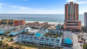 A coastal hotel complex with multiple buildings, including a tall hotel with a red and beige facade, and several smaller structures with blue roofs. - The Shore Thing - Gulf Shores (Gulf Shores)
