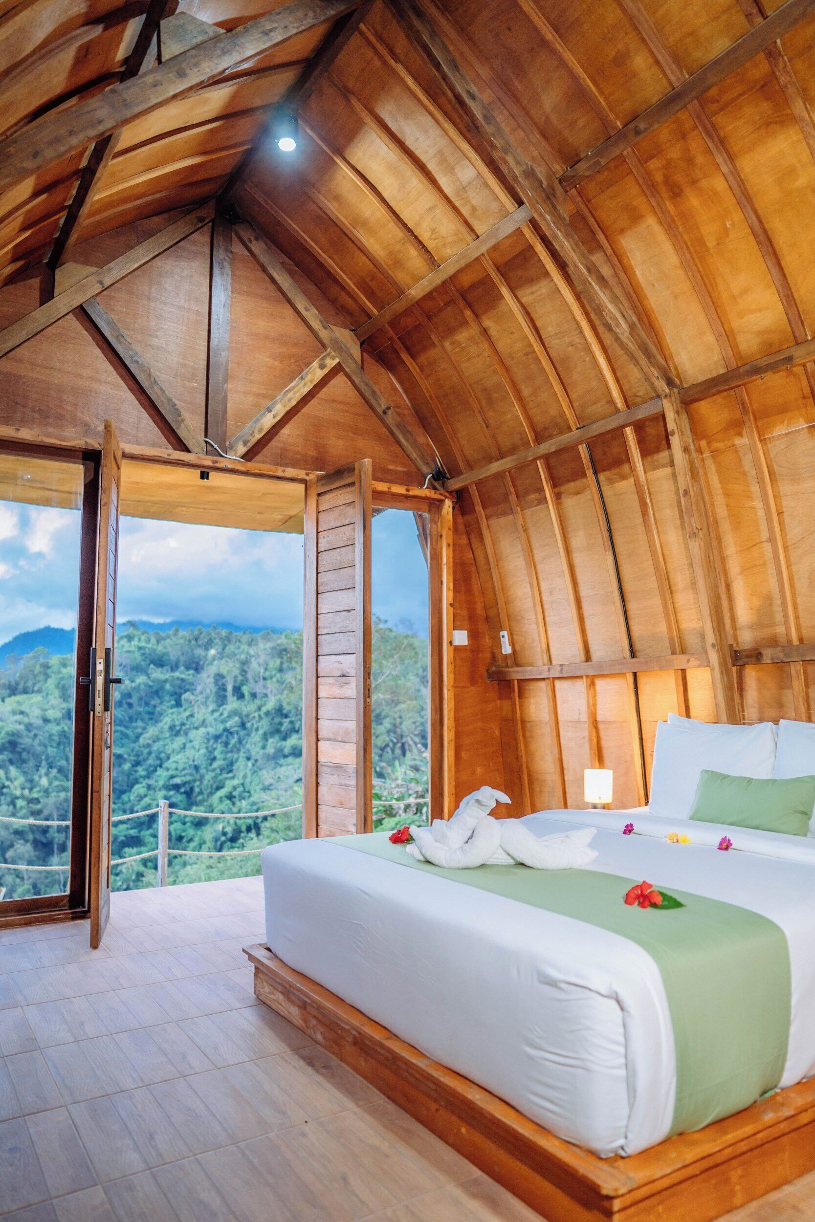 A bedroom with a large bed, wooden ceiling, and a view of a forested landscape.