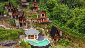 Un complexe hôtelier composé de plusieurs chalets en bois, entourés d’une végétation luxuriante, avec une piscine circulaire au centre et un escalier menant aux chalets.