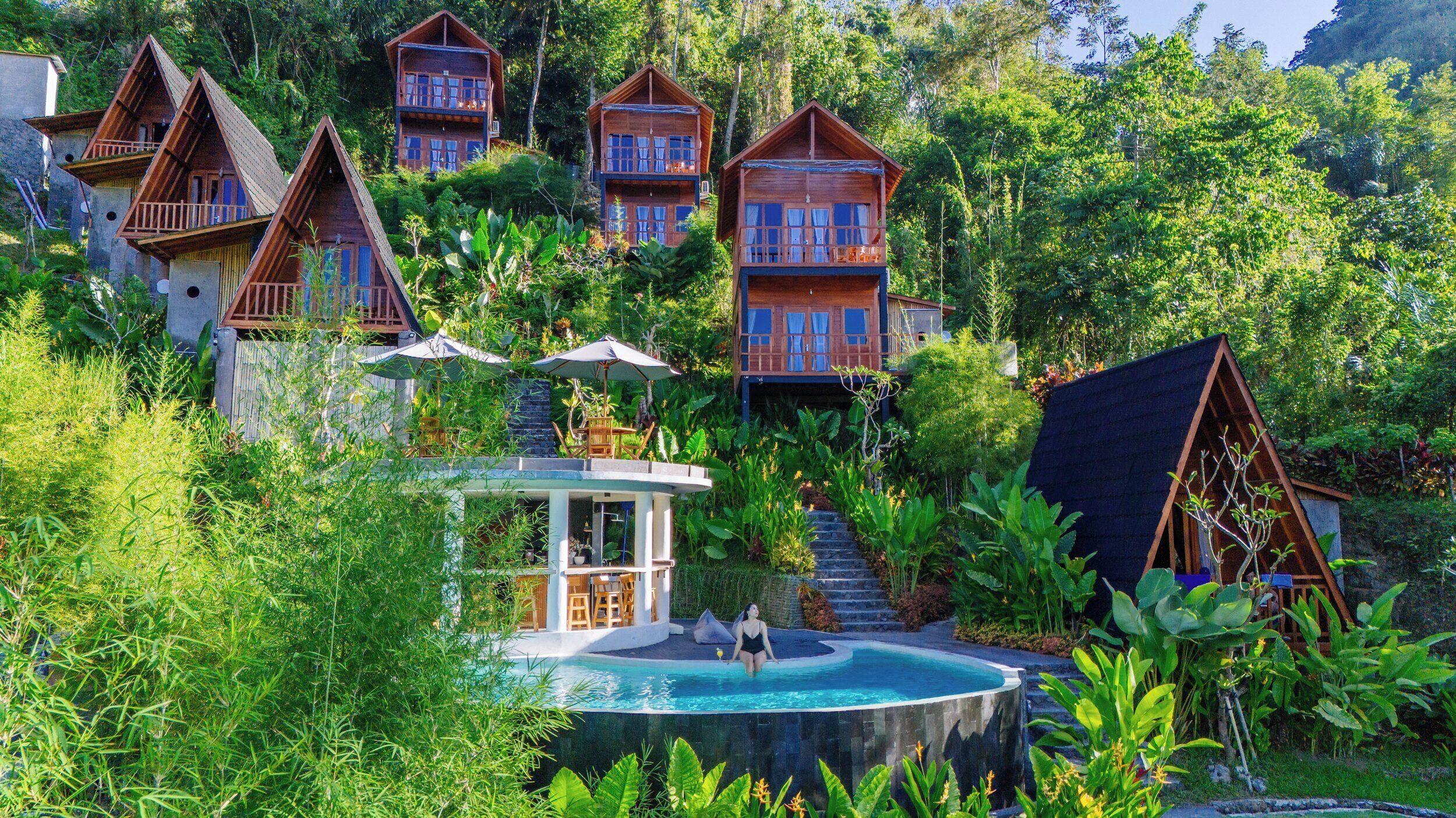 Ein Resort mit mehreren Holzhütten, einem Schwimmbad und üppiger Vegetation.