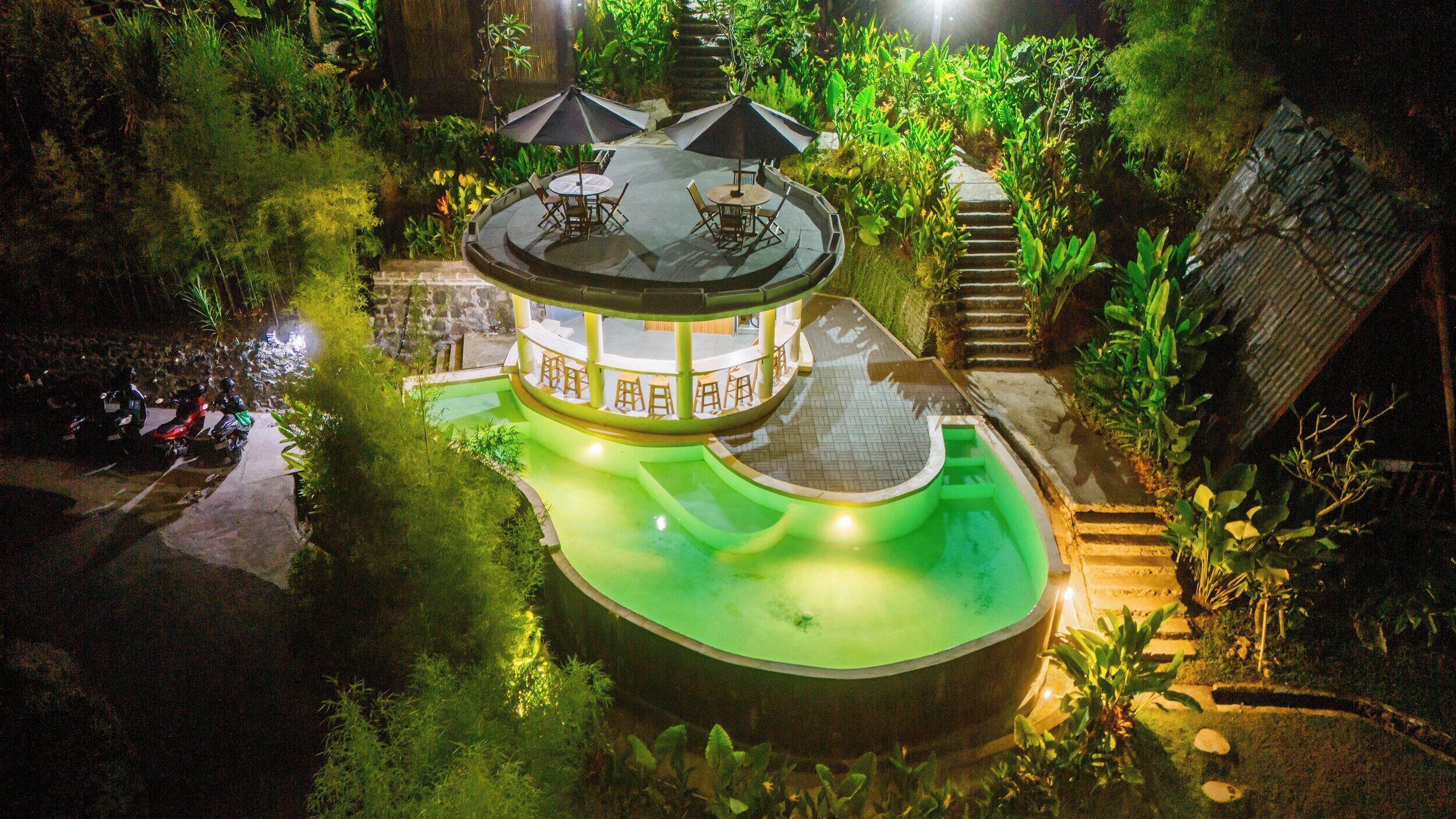 A circular building with a pool, surrounded by lush greenery.