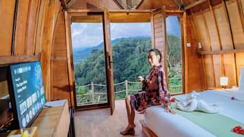 Una habitación de madera con una cama, un televisor y vistas a un paisaje boscoso.