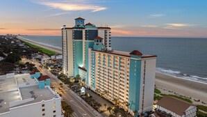 Un hôtel de grande hauteur, avec de nombreux étages, une vue sur la plage et un parking.