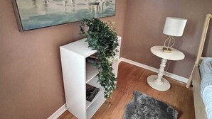 A bedroom with a sloped ceiling, a white console table with a plant, a round white side table with a lamp, a black furry rug, and a painting of sailboats on the wall. - Ideal Stay for City Explorers (Halifax)