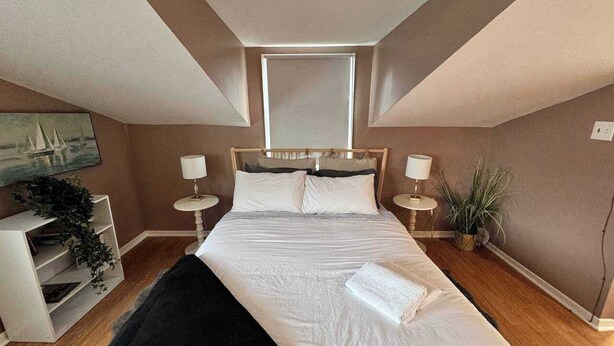 A bedroom with a large bed, two bedside tables with lamps, a window, and a plant. - Ideal Stay for City Explorers (Halifax)