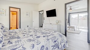 Ein Schlafzimmer mit Bett, Fernseher, Kommode, Deckenventilator und einer Glastür, die auf einen Balkon führt.