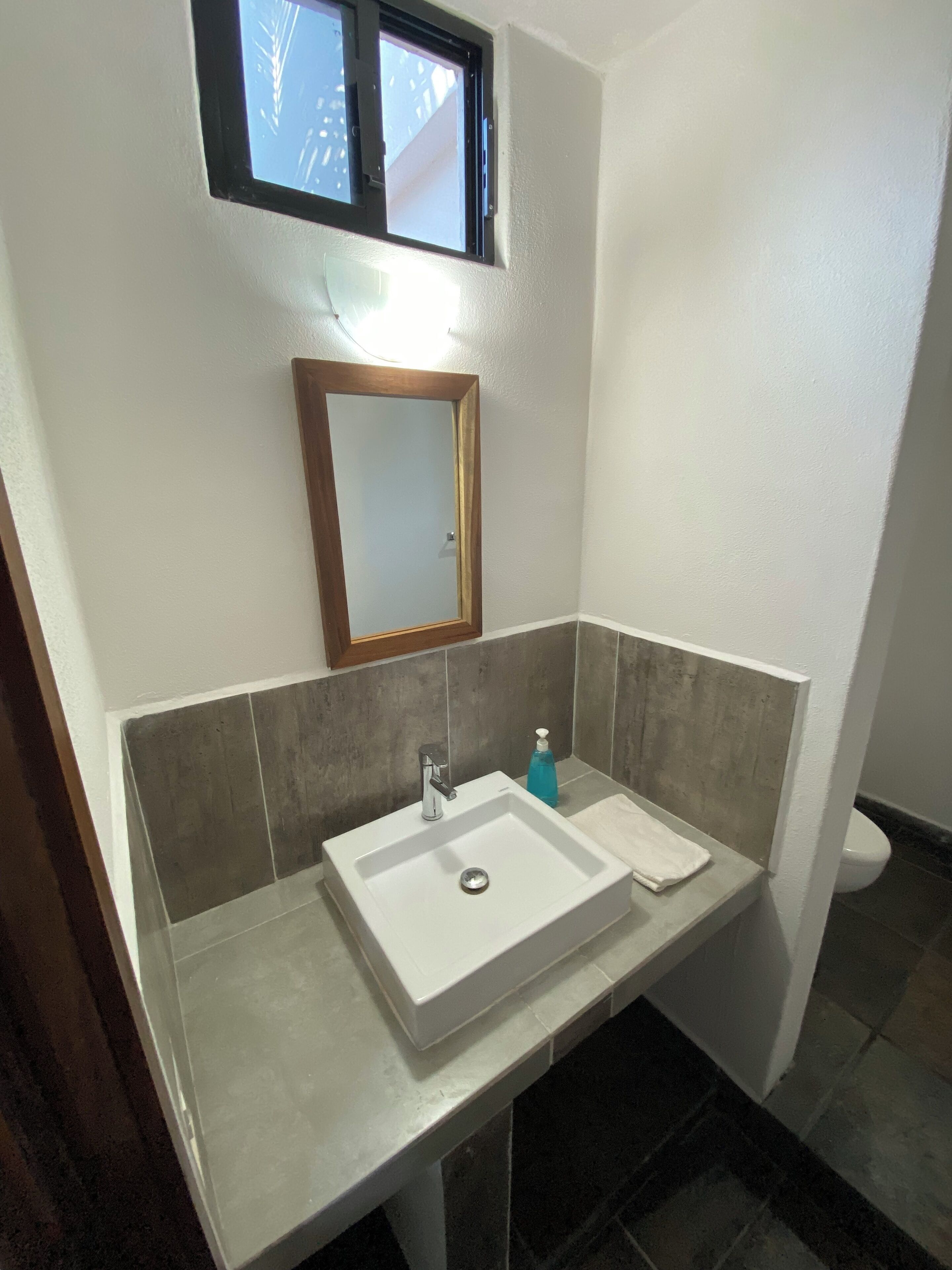A bathroom with a white sink, a mirror, and a window above the mirror.