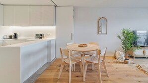 Een moderne keuken met witte kastjes, een houten eettafel met stoelen, een spiegel aan de muur en een televisie op een houten kast.