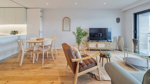 Een moderne woonkamer met een eethoek, een bank, een televisie en een groot raam.