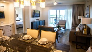 Hotellihuone, jossa on ruokailutila, olohuone sohvineen ja tuoleineen, parveke, jolta on näkymä, sekä seinälle asennettu televisio.