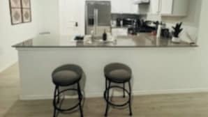 A modern kitchen with white cabinets, a central island with two stools, and a stainless steel refrigerator. - Opossum Trail (New Braunfels)