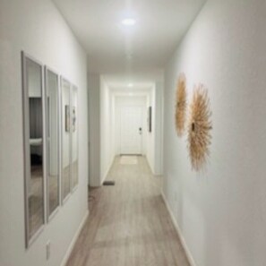 Un couloir avec un plancher de couleur claire, des murs blancs et une porte au fond.
