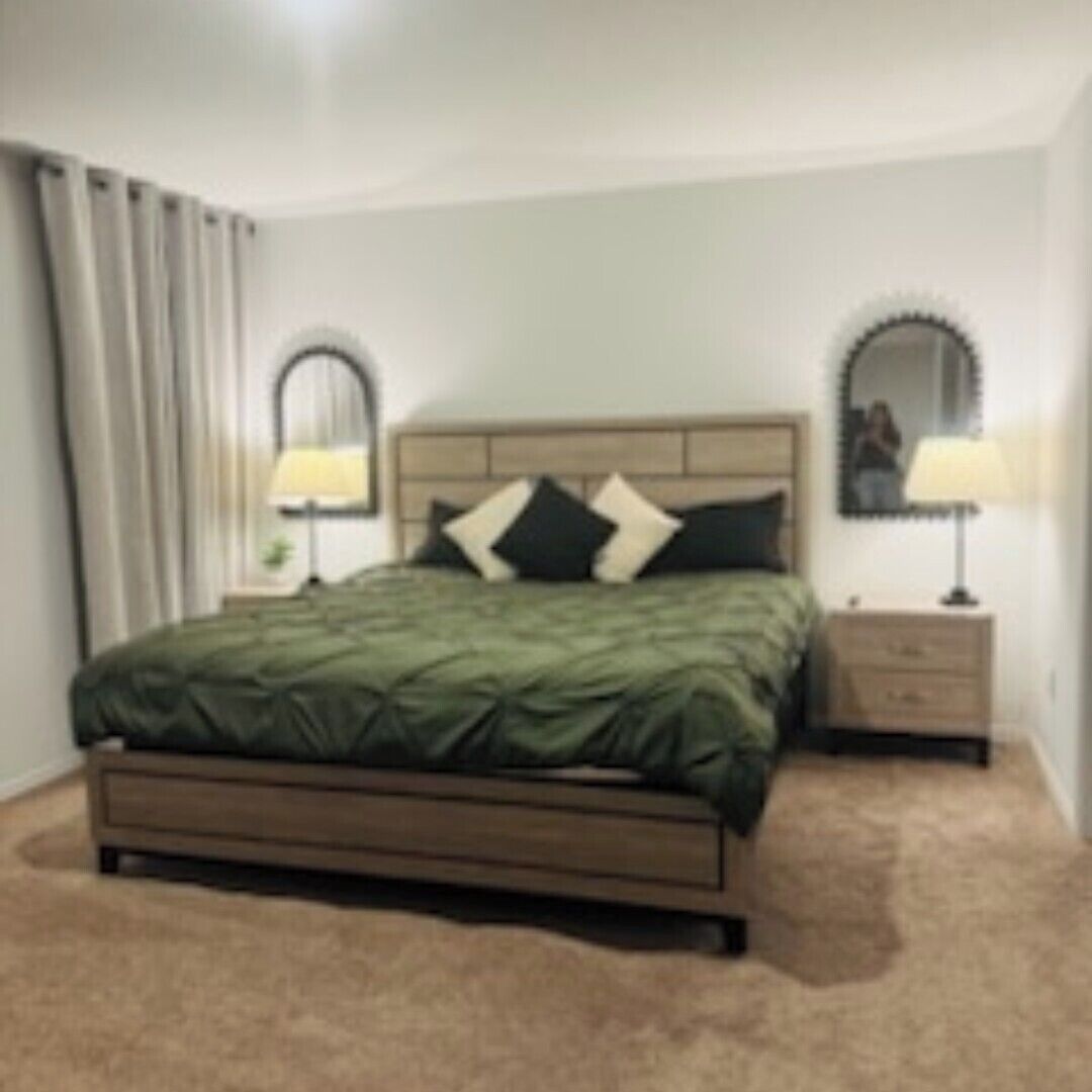 A neatly arranged bedroom with a bed, two bedside tables with lamps, a mirror, and a window with curtains.