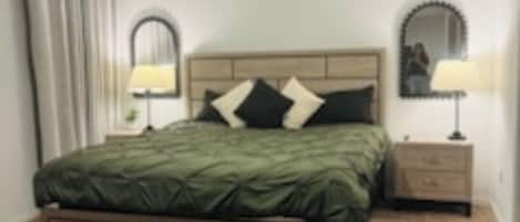 A neatly arranged bedroom with a bed, two bedside tables with lamps, a mirror, and a window with curtains.