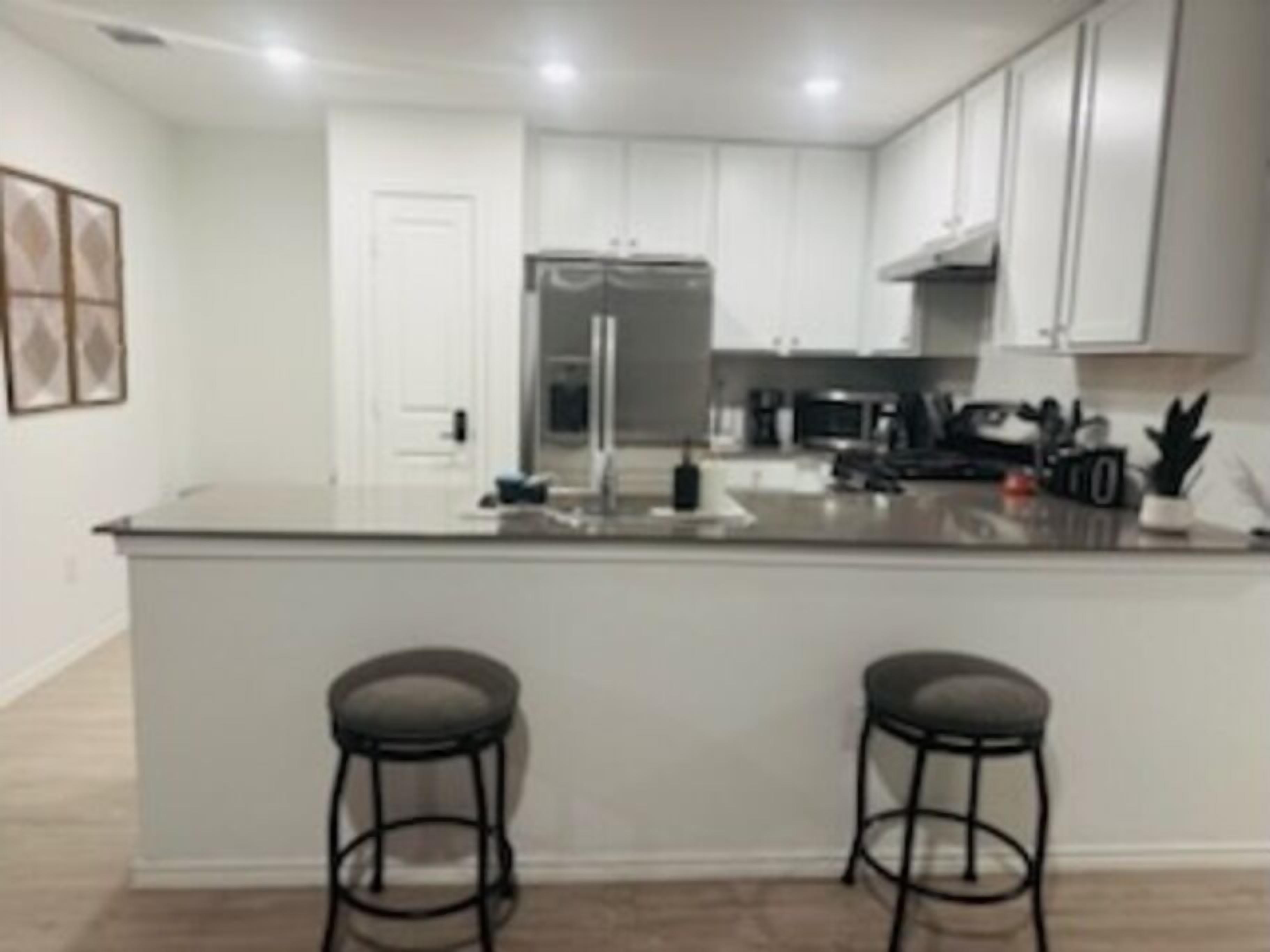A modern kitchen with white cabinets, a stainless steel refrigerator, and a central island with two bar stools.