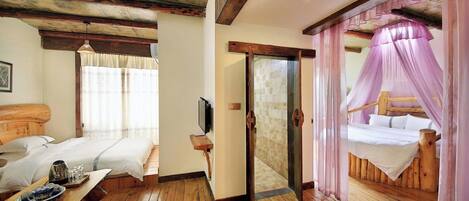 Una habitación con pisos de madera, una cama con dosel de madera, una mesita de noche con bandeja y un televisor en la pared.
