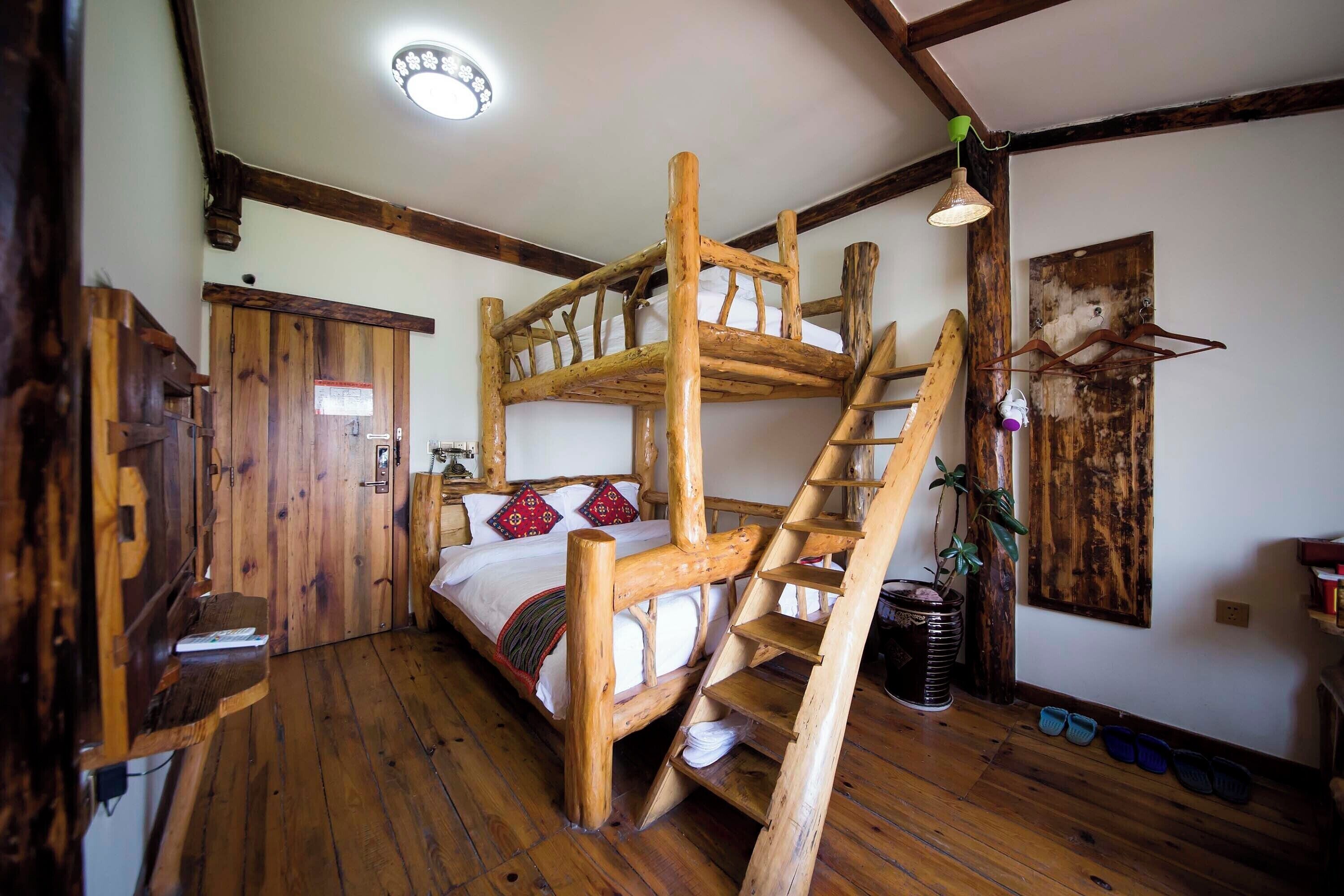 Uma cama beliche rústica de madeira com uma escada, uma porta de madeira e uma pequena prateleira com livros.