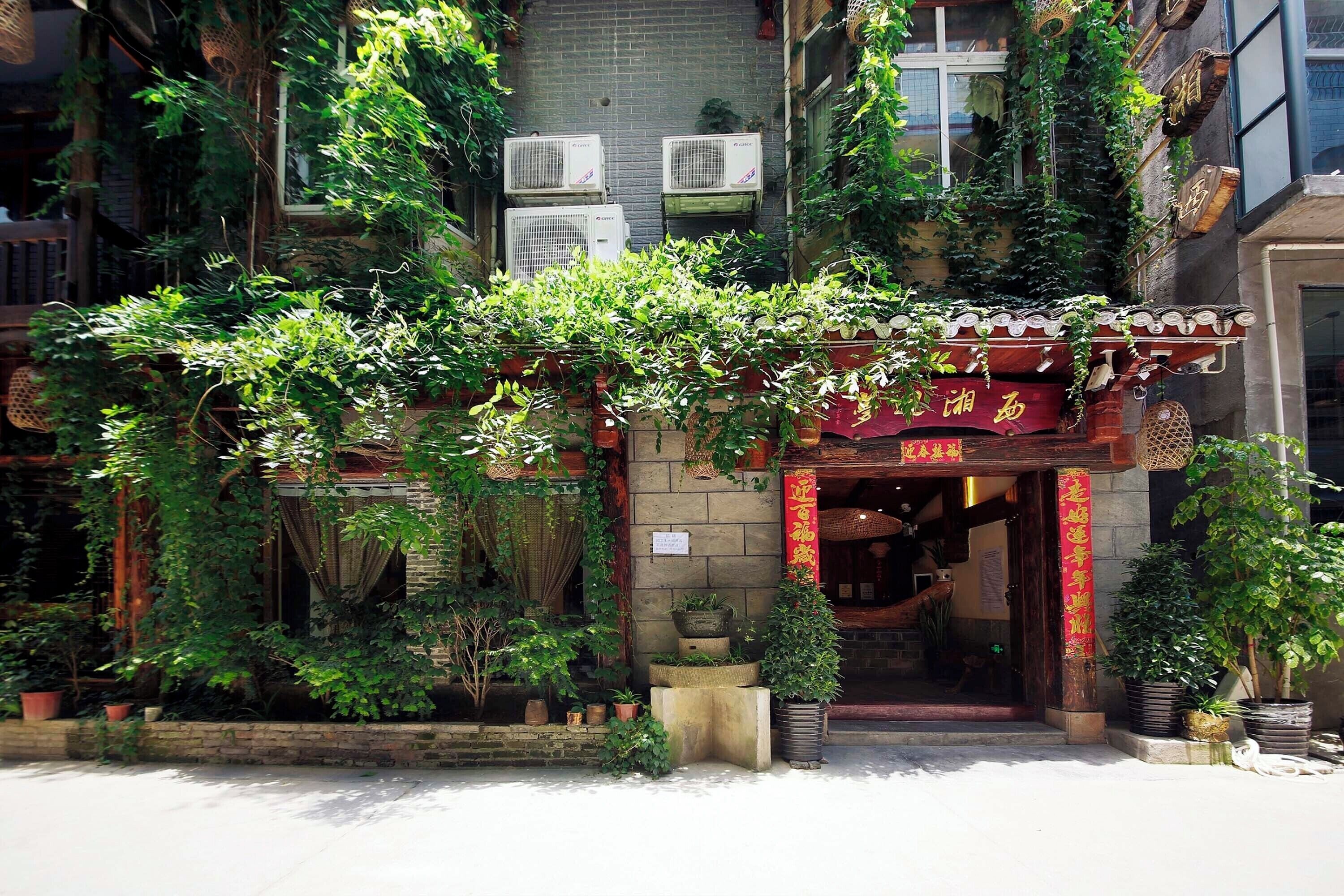 Un edificio tradicional con entrada de madera, plantas en macetas y unidades de aire acondicionado en la pared.