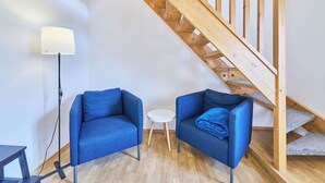A room with a wooden staircase, two blue armchairs, a small white table, and a floor lamp.