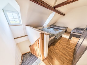 Ein Schlafzimmer im Loft-Stil mit schrägem Dach, Holzbalken, einem kleinen Fenster und einer Treppe.