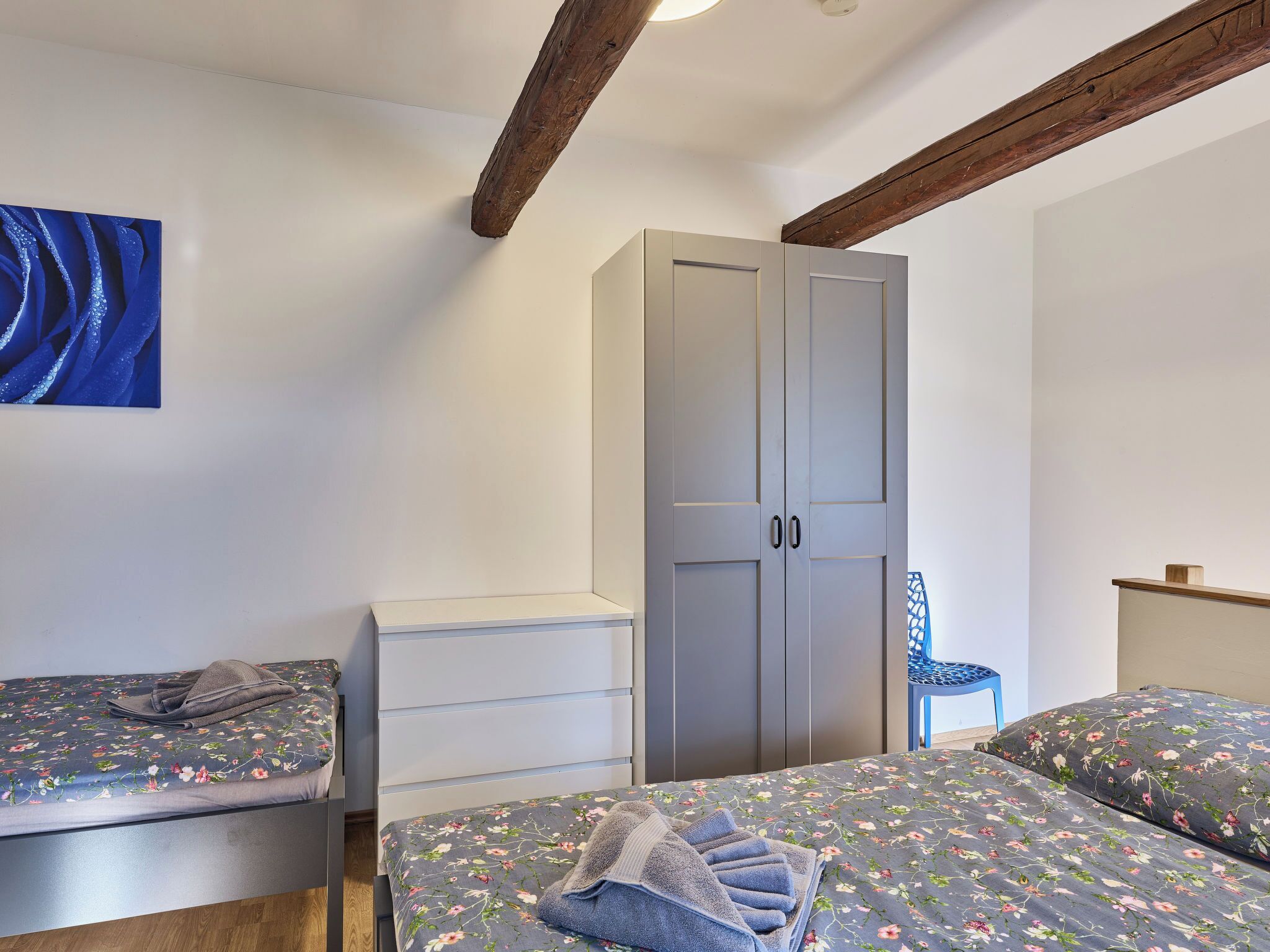 A bedroom with two beds, a wardrobe, a small table, and a chair.