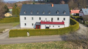 A large, multi-story building with a red-roofed section, surrounded by greenery and a clear sky.
