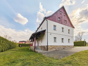Ein zweistöckiges Gebäude mit rotem Dach, weißen Wänden, einer Laube und einem Steinfundament.