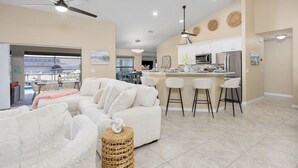 Una sala de estar moderna con un sofá blanco, una cocina con armarios blancos y un comedor con taburetes de bar.