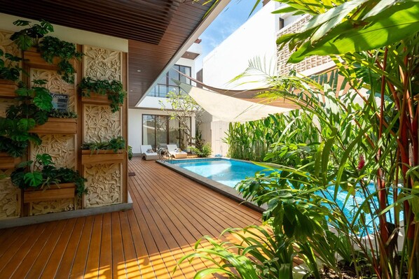 A wooden deck with a pool, surrounded by lush greenery and modern architecture. - Villa Hattala (Canggu)