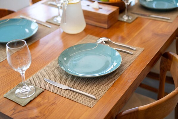 Una mesa de madera con un plato azul, una copa de vino y un cuchillo sobre un mantel individual.