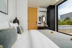 A modern bedroom with a large bed, a bedside table with a mirror, a wardrobe, and a view of an outdoor seating area. - Villa Sapta (Cemagi)