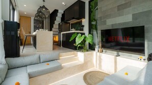 A modern living room with a sectional sofa, a flat-screen TV, and a staircase leading to a kitchen area. - Villa Sapta (Cemagi)