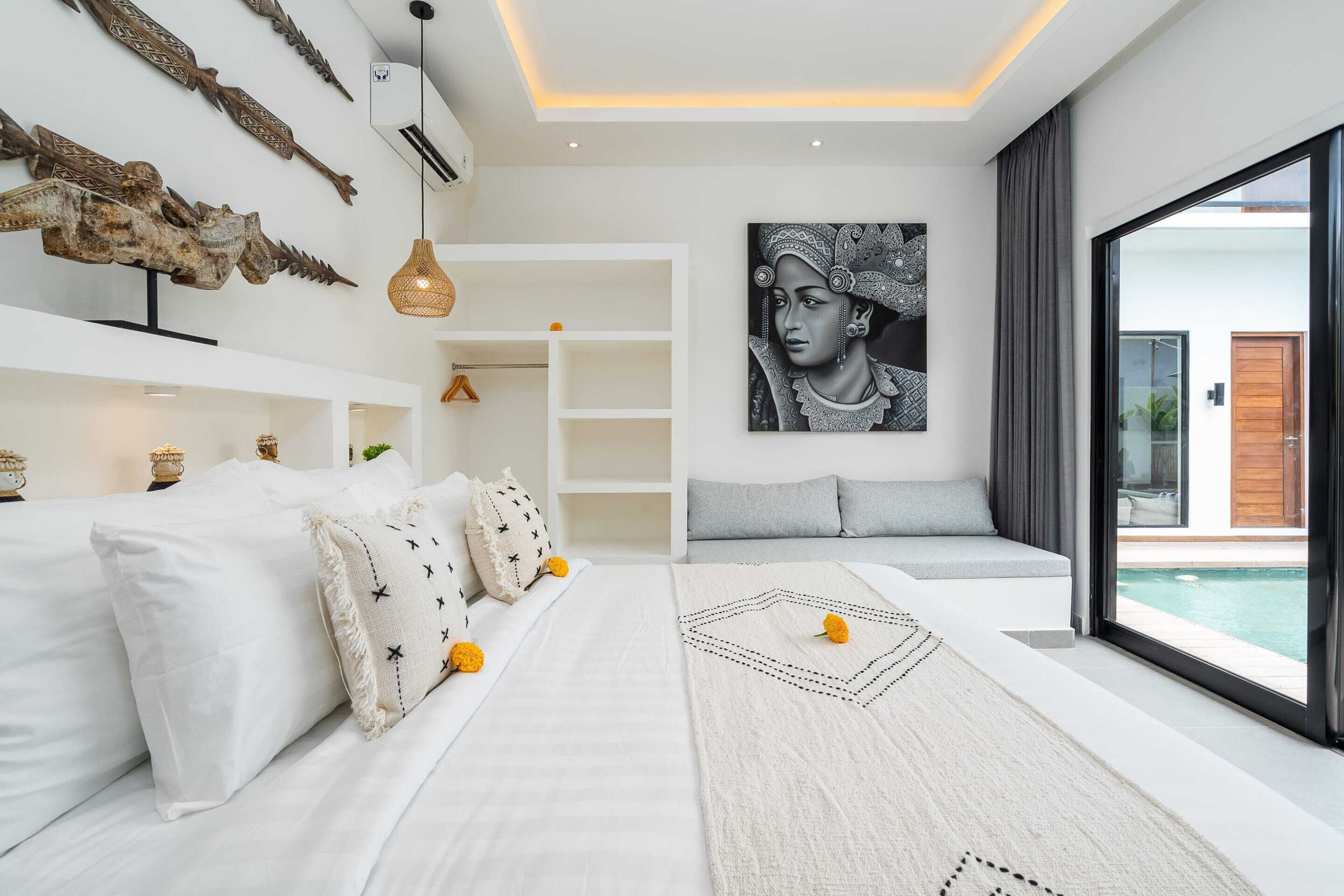 A modern bedroom with a large bed, a seating area, a painting, and a view of the outdoors.