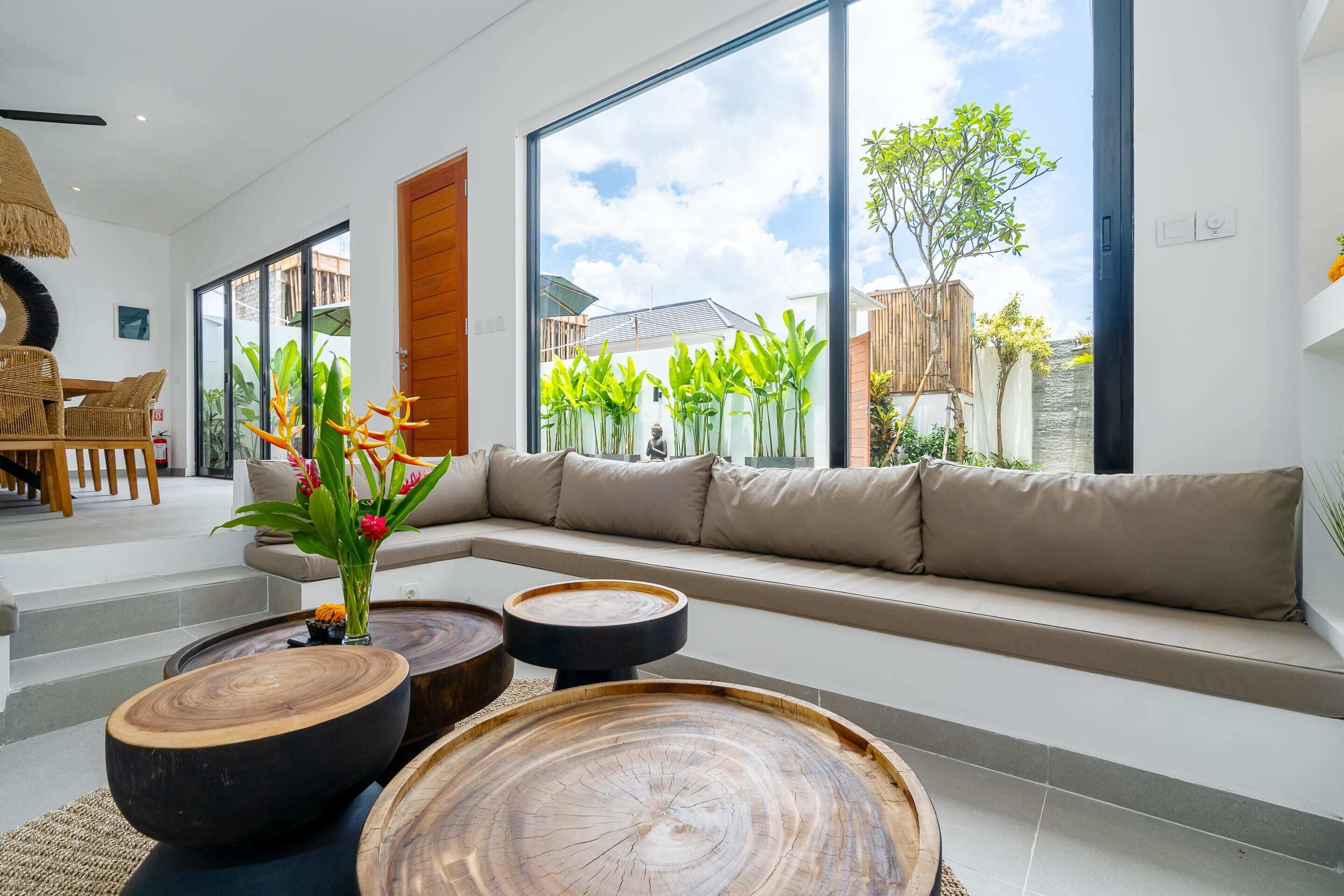 A modern living room with a large window, a wooden coffee table, a sofa, and a wicker chair.