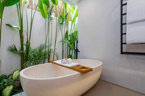 A modern bathroom with a freestanding bathtub, a wooden tray with towels, and lush green plants. - Villa Sevu 8 (Cemagi)